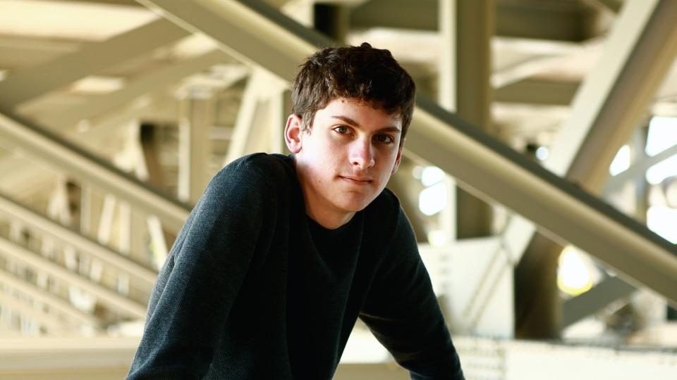Reactive Attachment Disorder Criteria hero image of a teenage boy sitting while looking at the viewer.