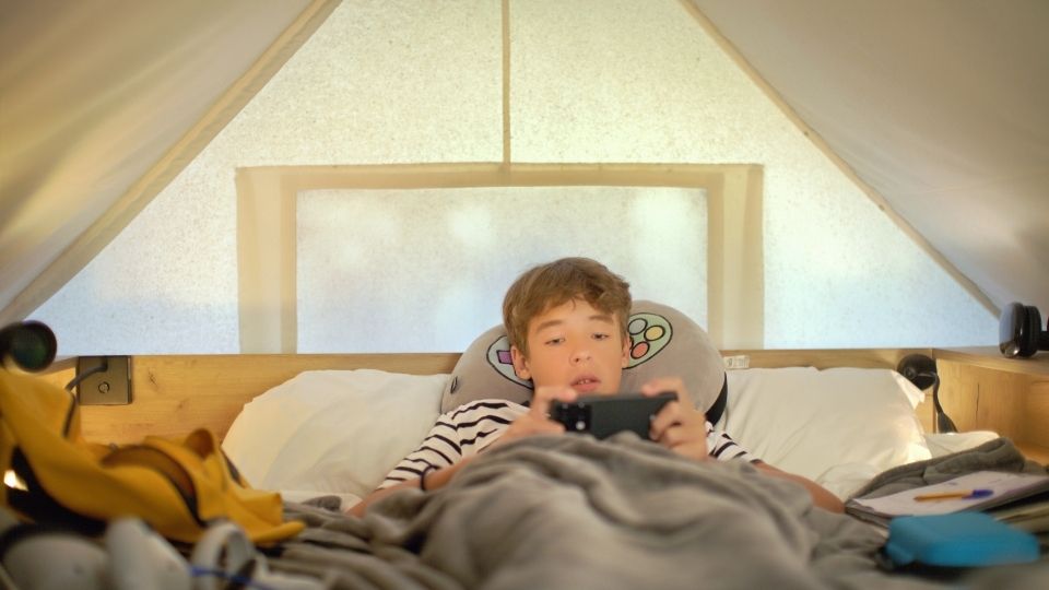 A boy playing on his phone in bed demonstrates one way OCD in teens can manifest